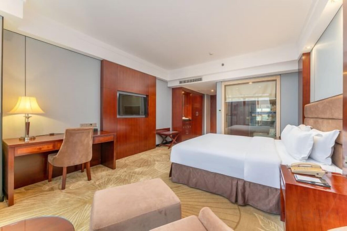 A hotel room with a bed, desk, chair, and a television.