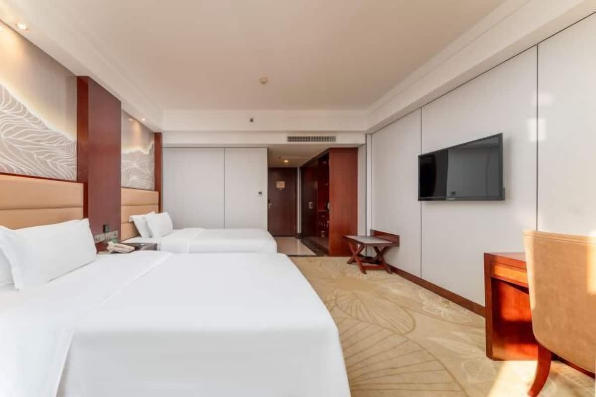 A hotel room with two beds, a TV, a desk, and a chair.