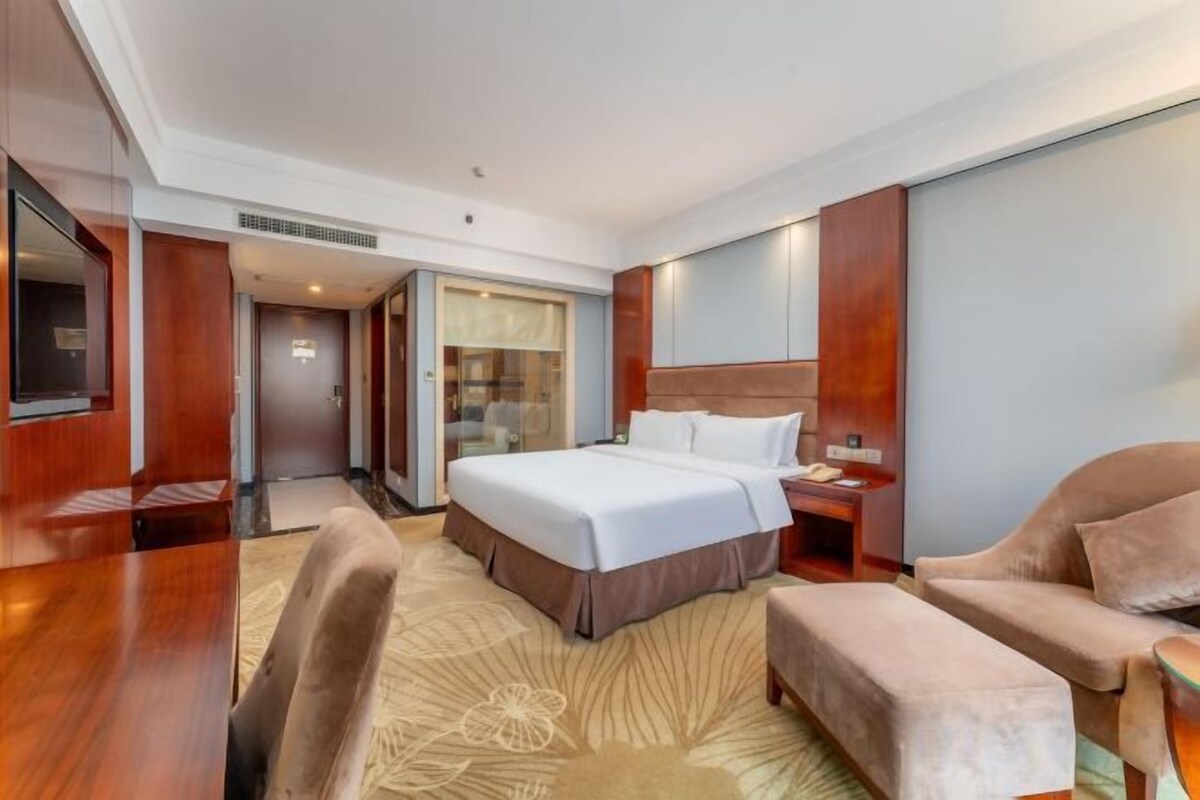 Una camera d'albergo con un letto grande, una zona salotto con una poltrona, una scrivania e un televisore.