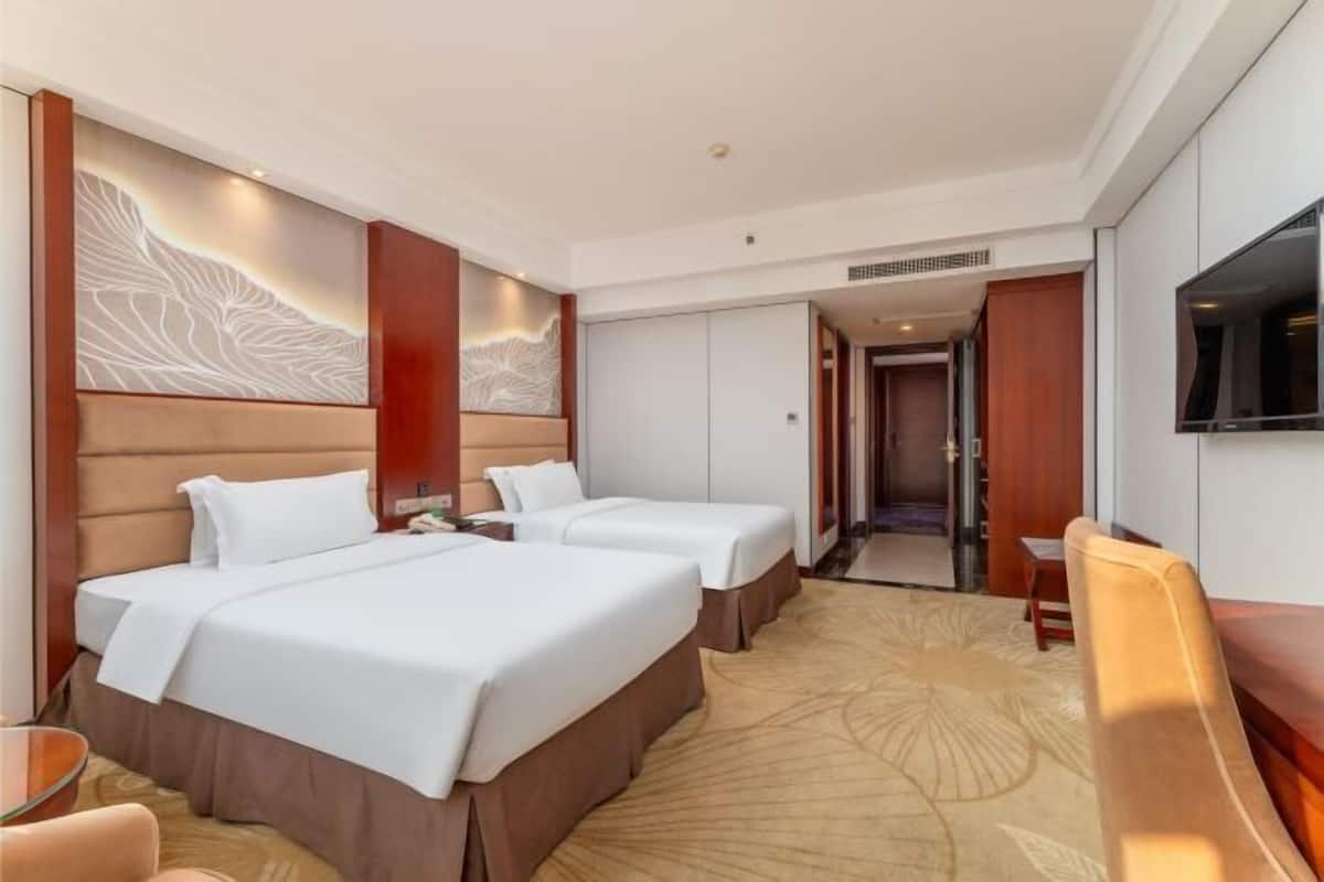 A hotel room with two beds, a TV, and a desk.