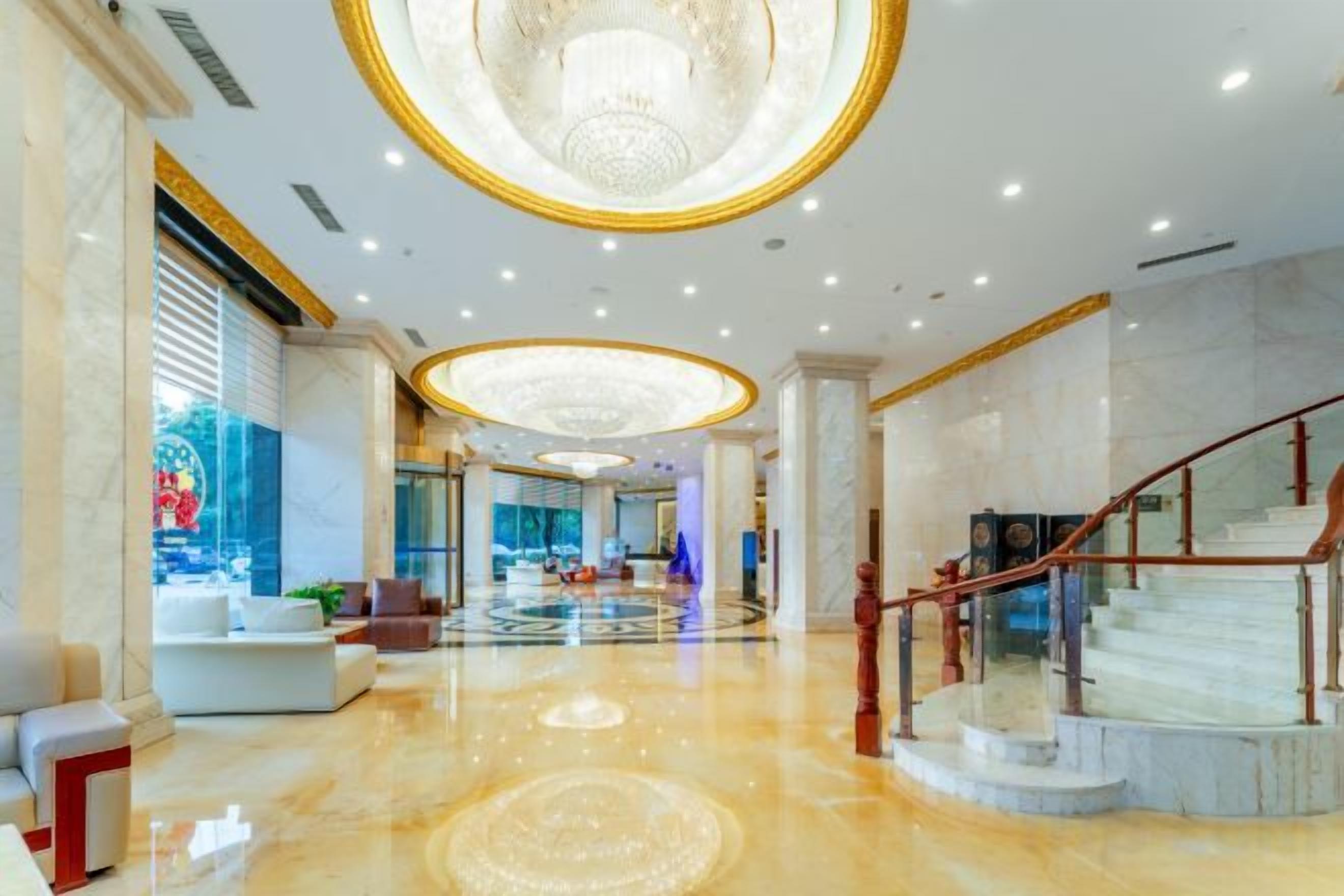 A spacious lobby with a marble floor, a grand chandelier, and a staircase with a red railing.