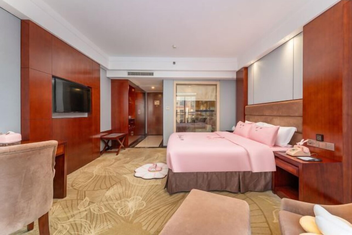 A hotel room with a bed, a desk, a chair, a television, and a bathroom visible through an open door.