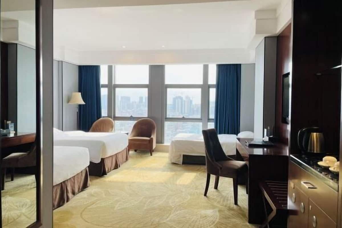 A hotel room with two beds, a desk, a chair, a television, and a view of the city.