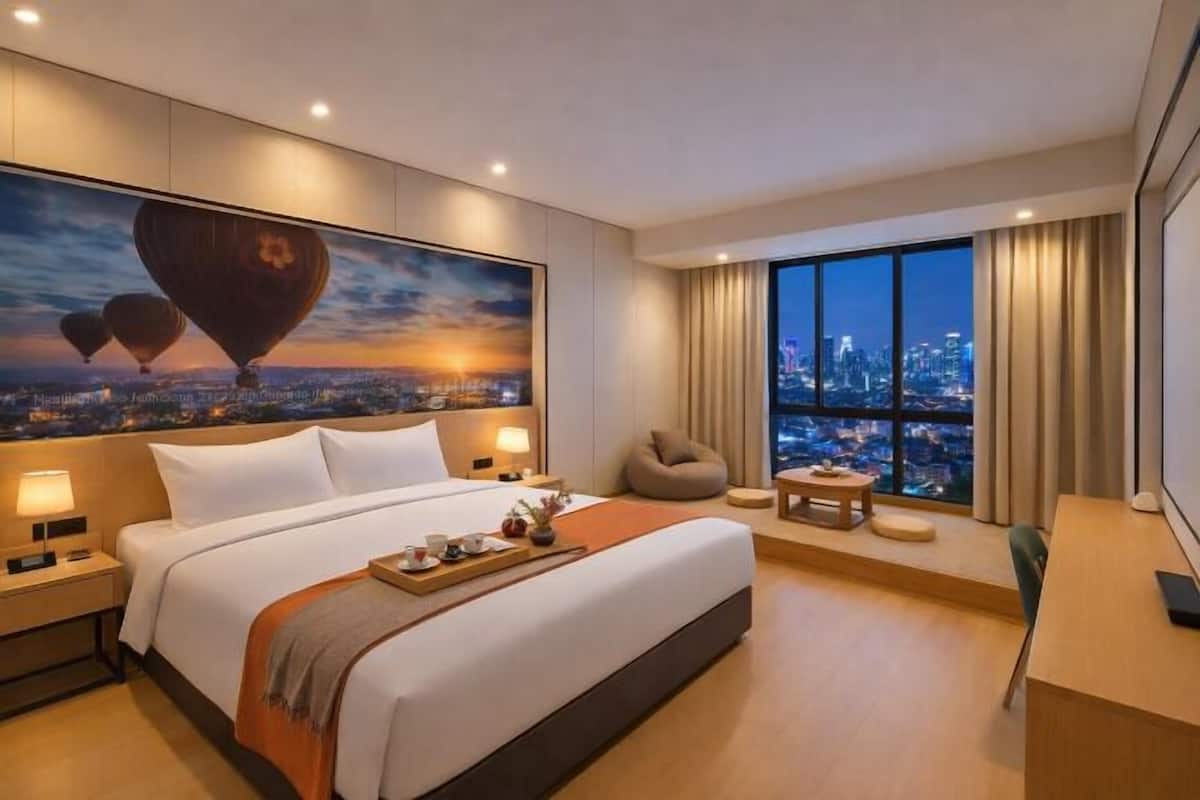 Habitación de hotel con una cama grande, un escritorio, una silla, vista de la ciudad y un cuadro con globos aerostáticos.