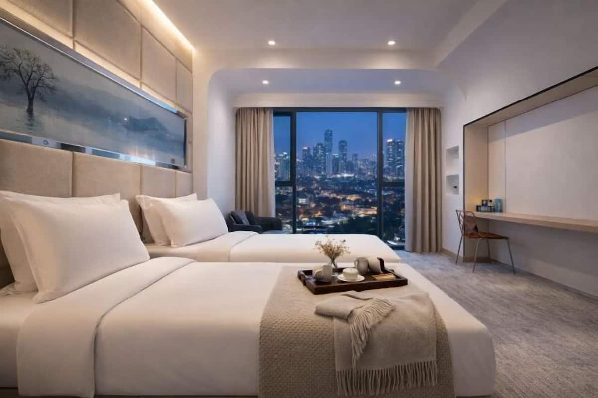 Una habitación de hotel moderna con dos camas, un escritorio, una silla y un ventanal con vistas a la ciudad.