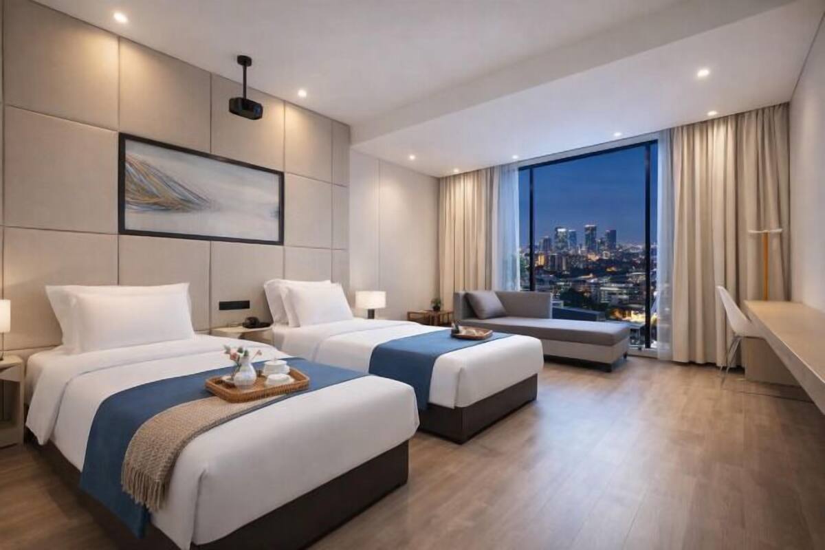 Una habitación de hotel moderna con dos camas, un sofá, vistas a la ciudad y un ventanal grande.