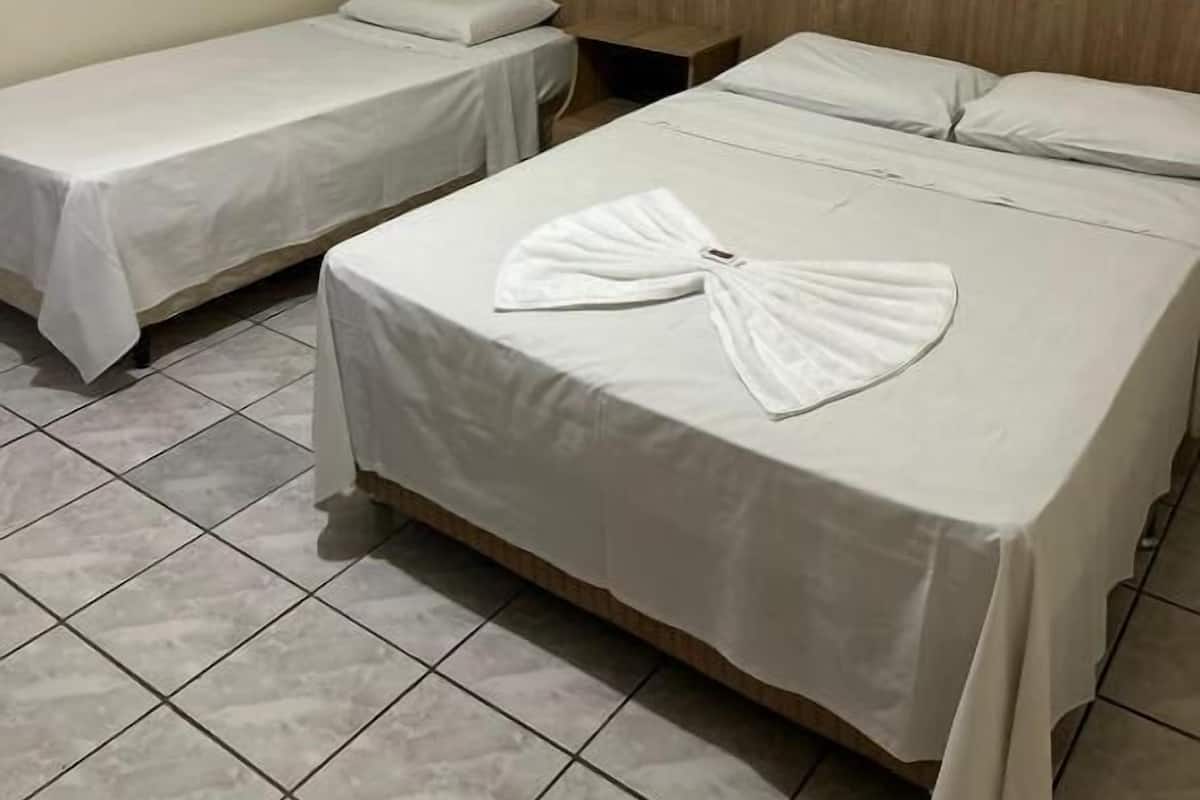 A hotel room with two single beds and one double bed, all with white linens.