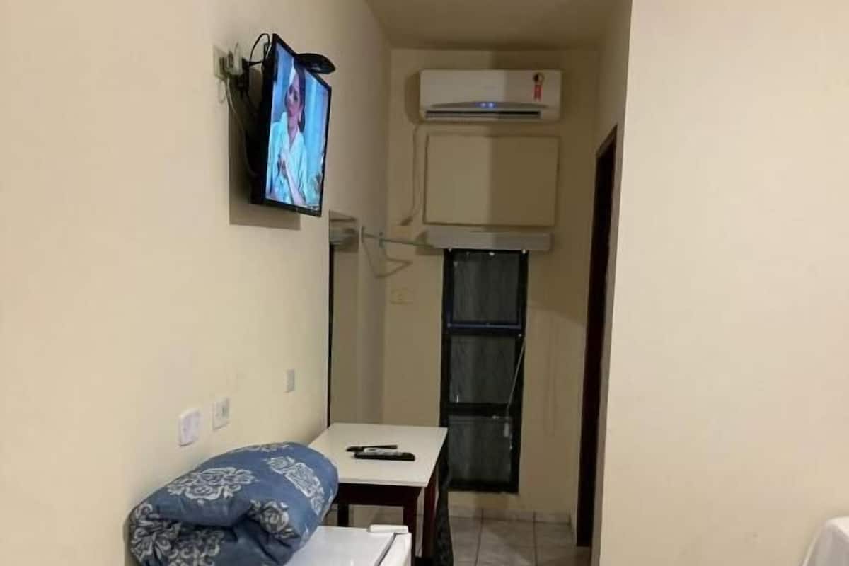 A small, compact room with a bed, a desk, and a television mounted on the wall.