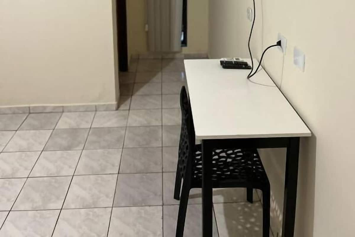 A small room with a white table and black chairs, a mounted TV on the wall, and an air conditioning unit above the door.