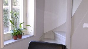 Un sillón de cuero negro con dos cojines, uno con texto, situado junto a una ventana con vistas a la vegetación.
