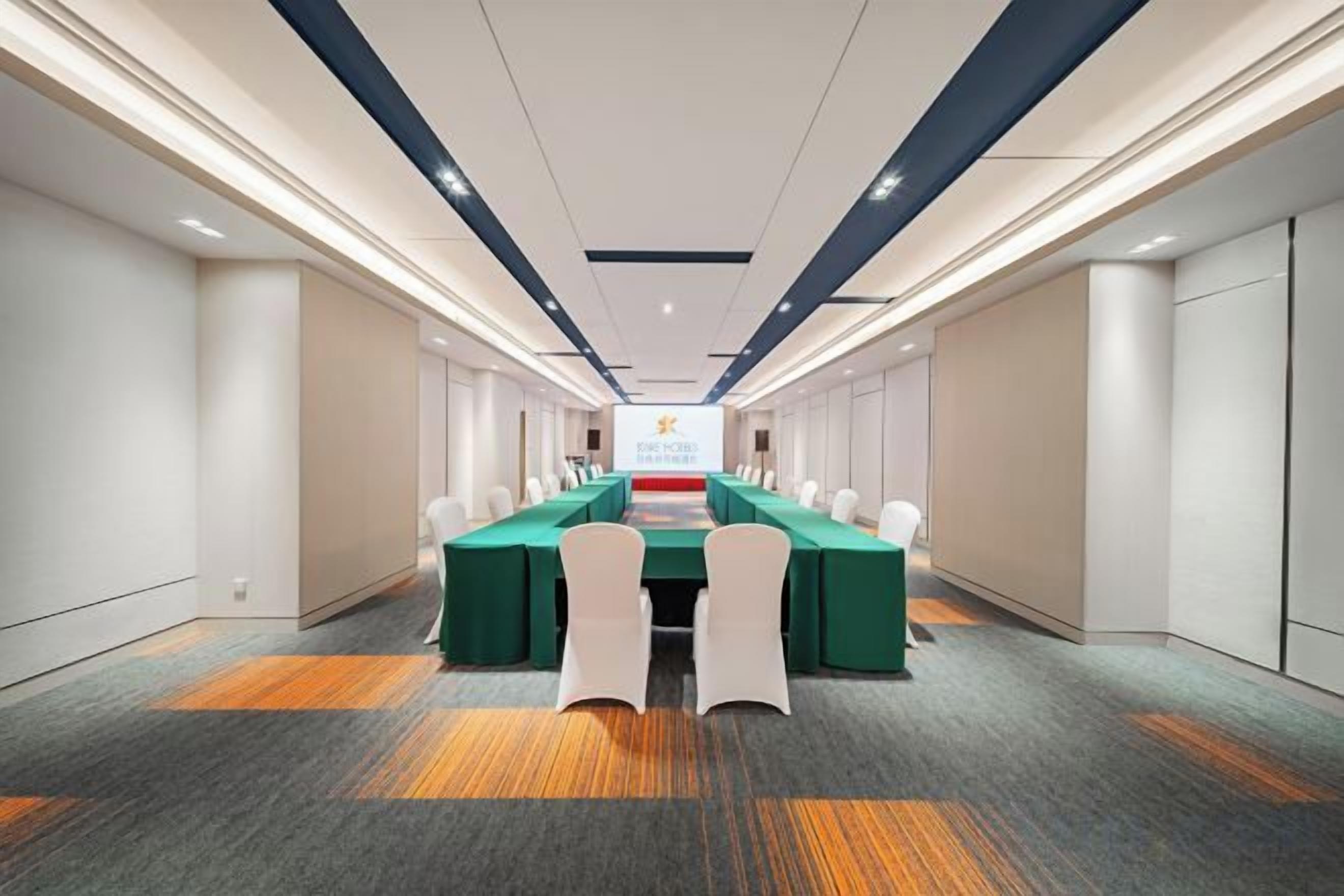 Un salón de conferencias con una mesa larga, sillas y una pantalla para presentaciones.