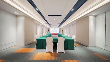 Un salón de conferencias con una mesa larga, sillas y una pantalla para presentaciones.