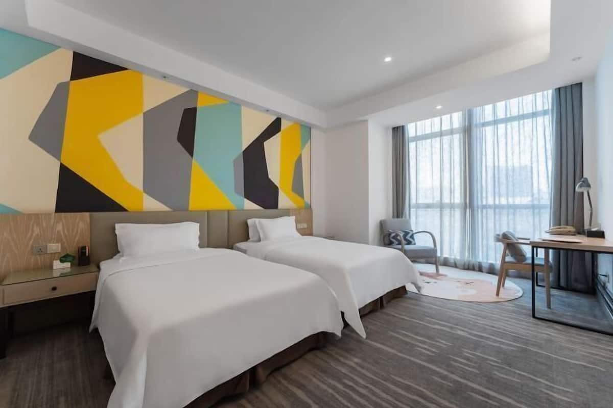 Una habitación de hotel con dos camas, un escritorio, una silla y un ventanal amplio.