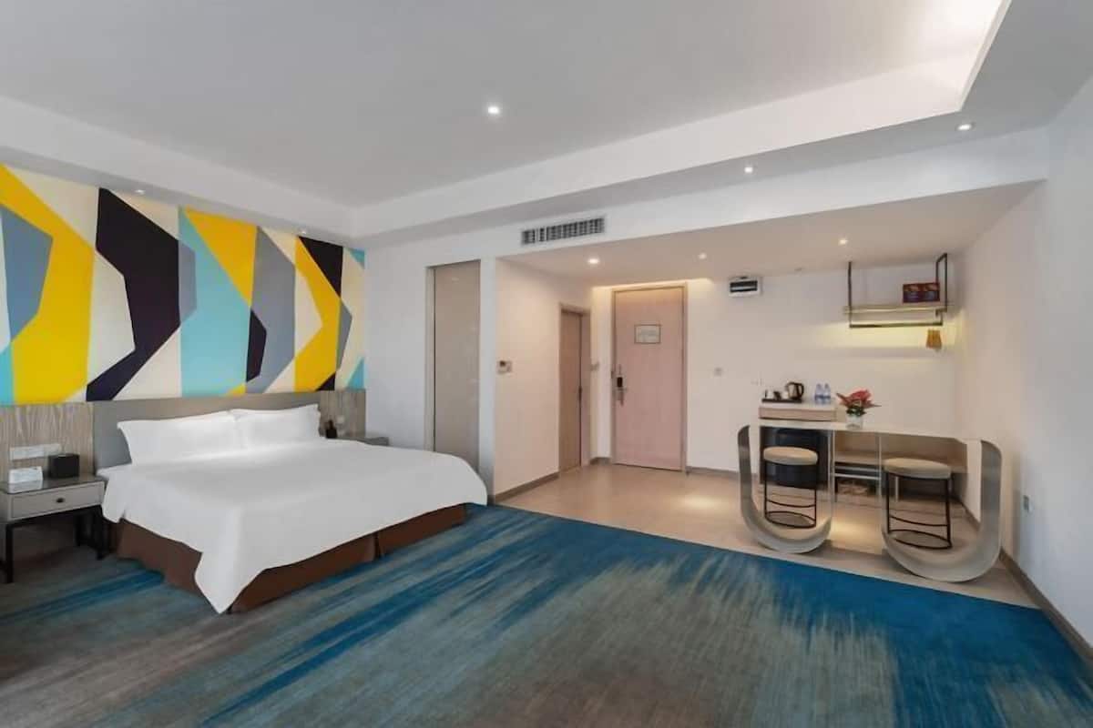 Habitación de hotel con cama, escritorio, silla, una pequeña mesa con un florero y un muro con diseños geométricos.