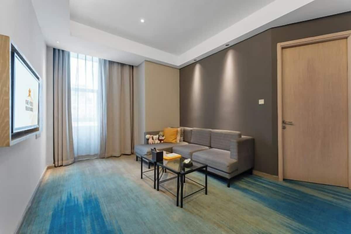 Una sala moderna con un sofá gris, una mesa de centro y un amplio ventanal con cortinas.