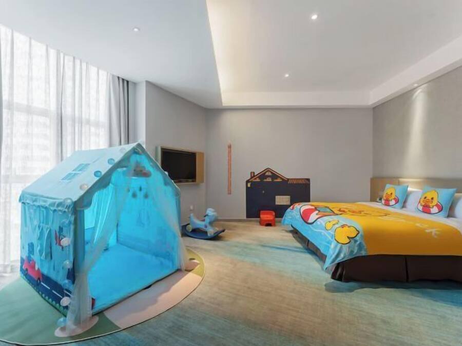 A hotel room with a bed, a play tent, a TV, and a window with curtains.