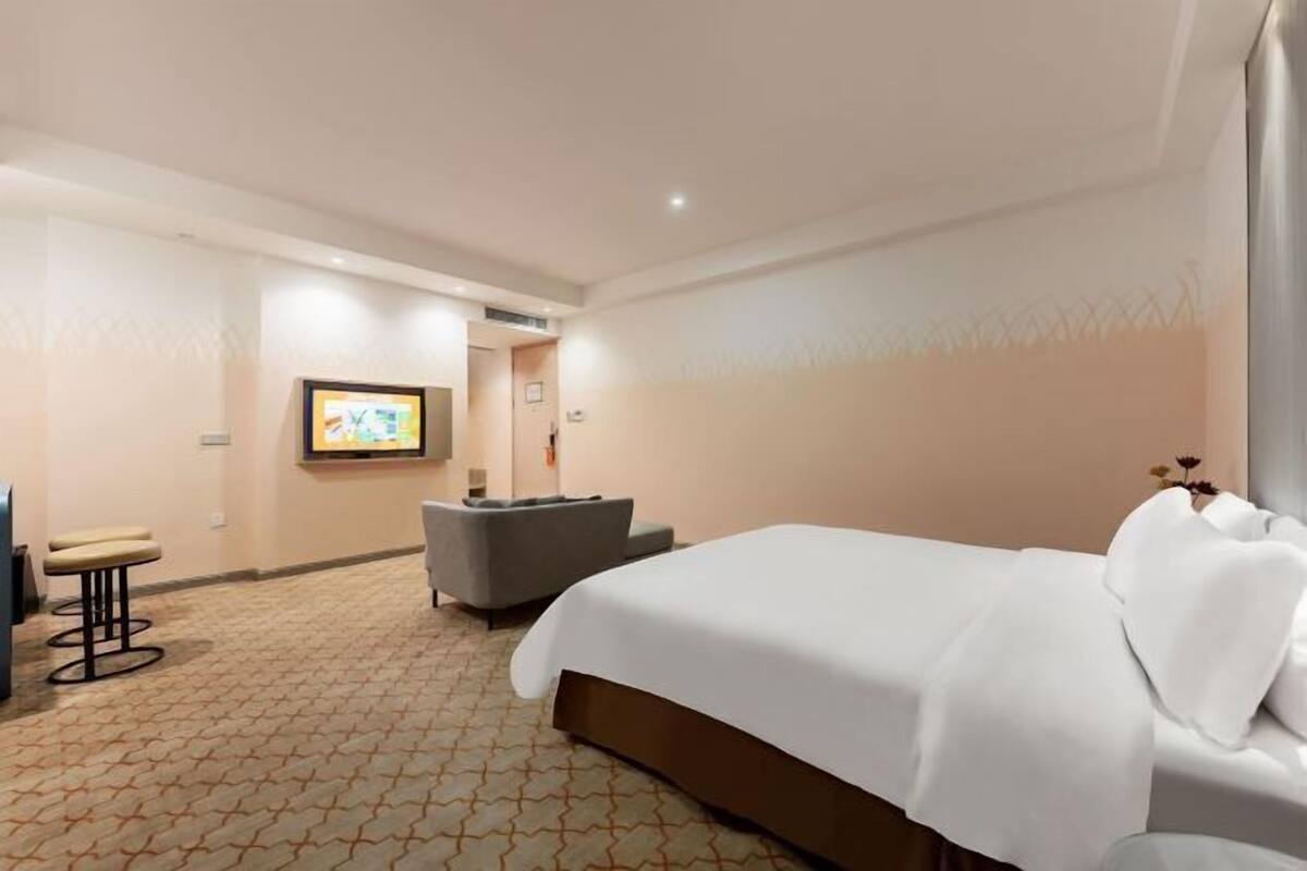Una habitación de hotel con cama, zona de estar, televisor y una obra de arte colgada en la pared.