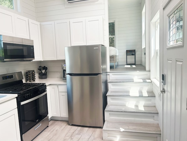 A modern kitchen with white cabinetry, stainless steel appliances, and a wooden floor.