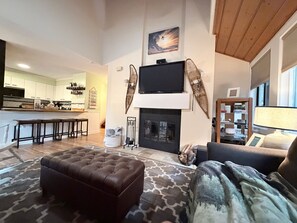 Ein Wohnzimmer mit Kamin, einem darüber montierten Fernseher und einer Küche im Hintergrund.