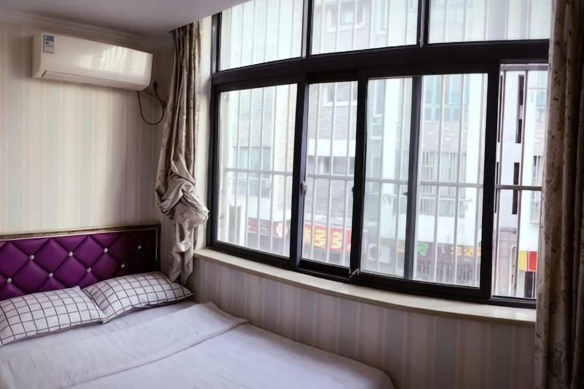 A bedroom with a bed, a window with curtains, and an air conditioning unit.
