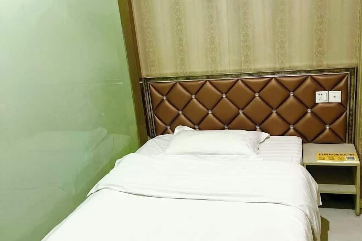 A single bed with a tufted headboard, a bedside table, and a wall with a patterned curtain.