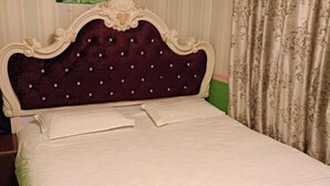 Una cama con cabecera capitonada, ropa blanca y pared verde.