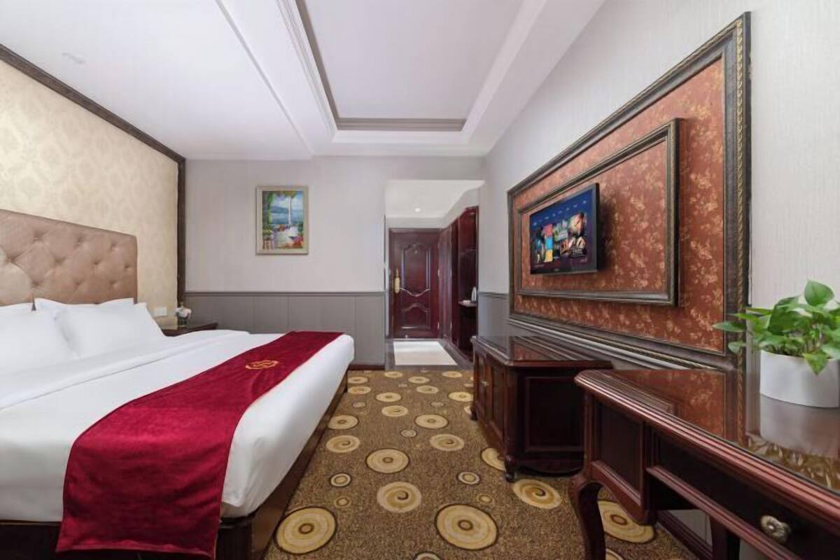 A hotel room with a large bed, a desk, a television, and a door leading to another room.