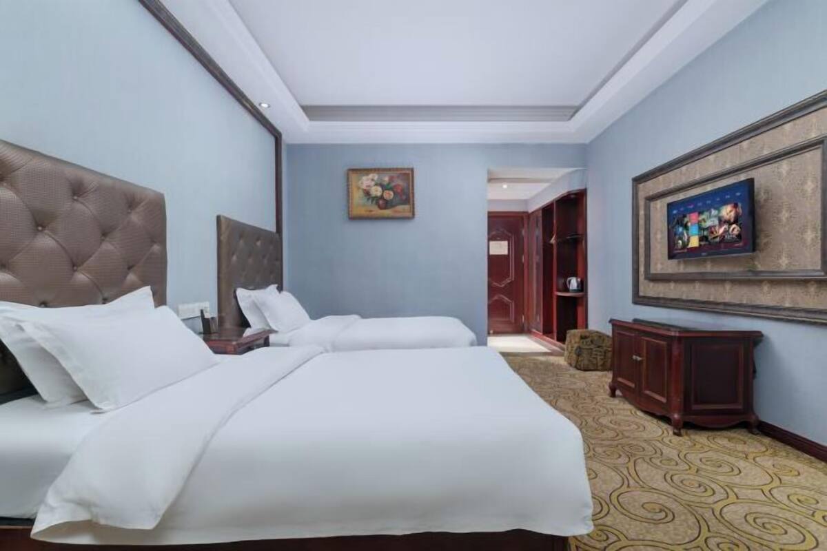 A hotel room with a large bed, a television, a painting, and a carpeted floor.