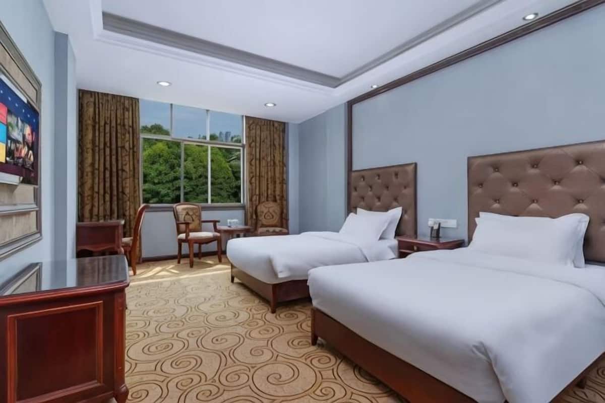 A hotel room with two beds, a desk, a chair, and a large window with curtains.