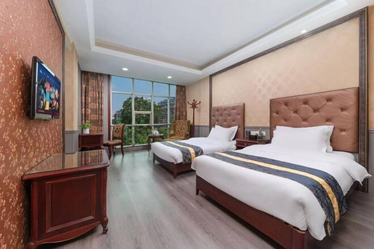 A hotel room with two beds, a desk, a chair, and a large window.
