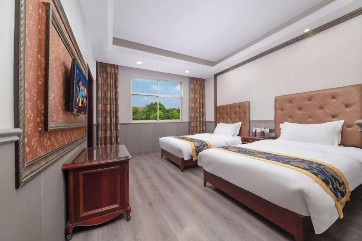 A hotel room with two beds, a TV, a window with a view, and a wooden floor.