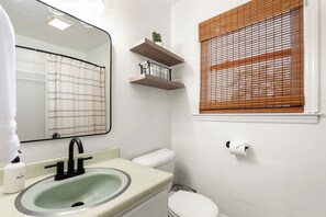 Ein Badezimmer mit Waschbecken, Toilette und einem Fenster mit Jalousien.