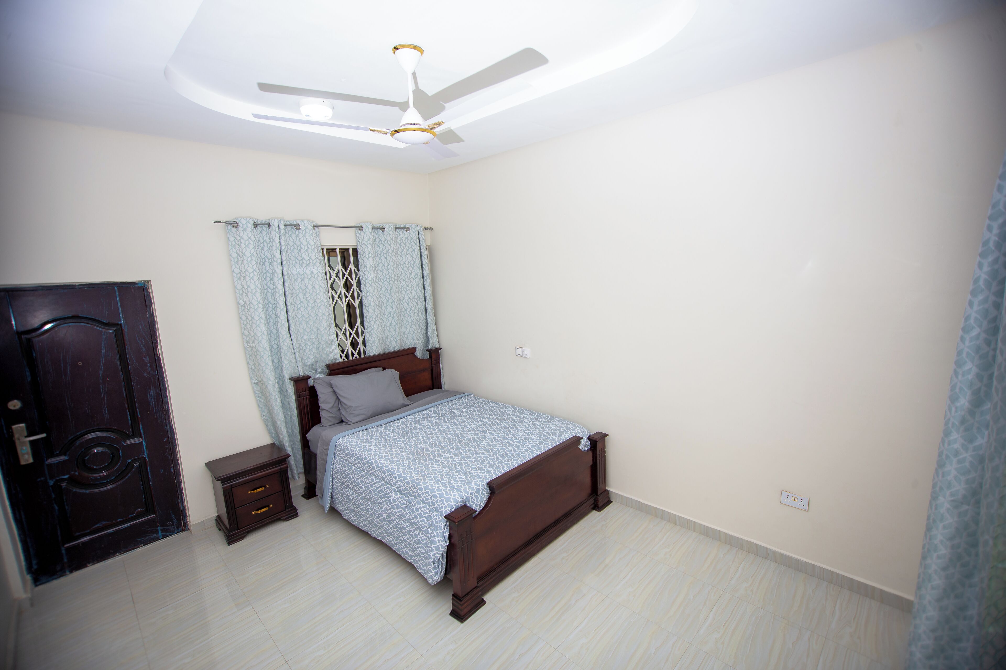 A bedroom with a bed, a nightstand, a ceiling fan, and a door.