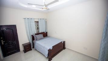 A bedroom with a bed, a nightstand, a ceiling fan, and a door.