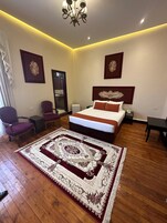 Une chambre à coucher avec un grand lit, deux fauteuils, un tapis et un lustre.