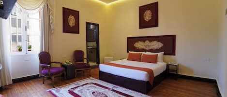 A hotel room with a large bed, a desk, a chair, and a view of the outside.