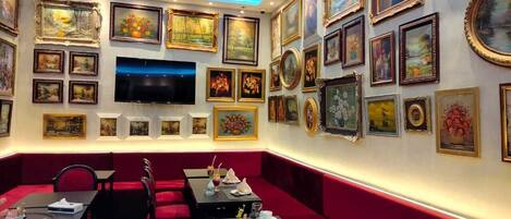 A restaurant with red booths, a TV mounted on the wall, and various framed artworks on the walls.