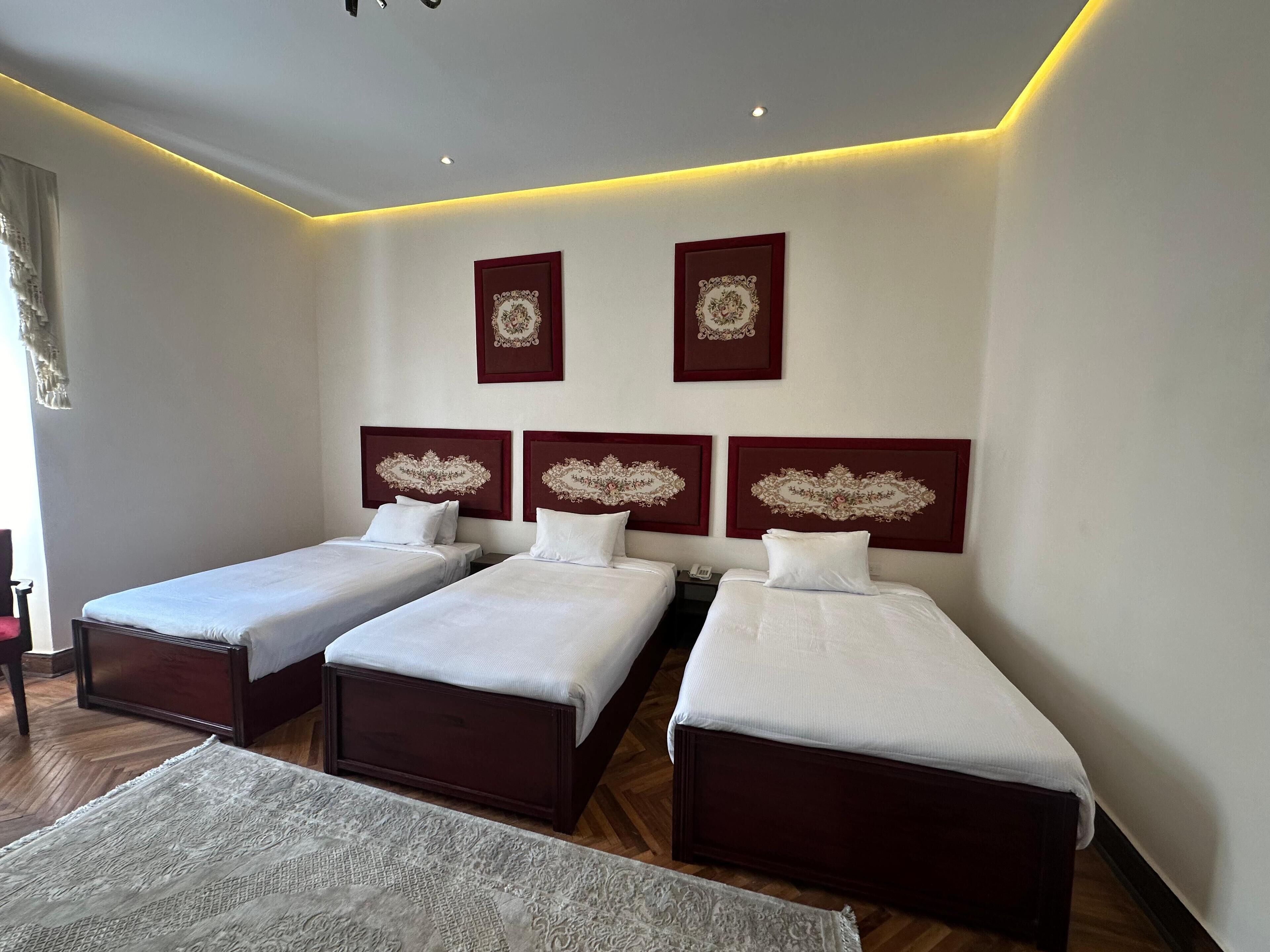 Quarto de hotel com três camas de solteiro, piso de madeira e um tapete grande.