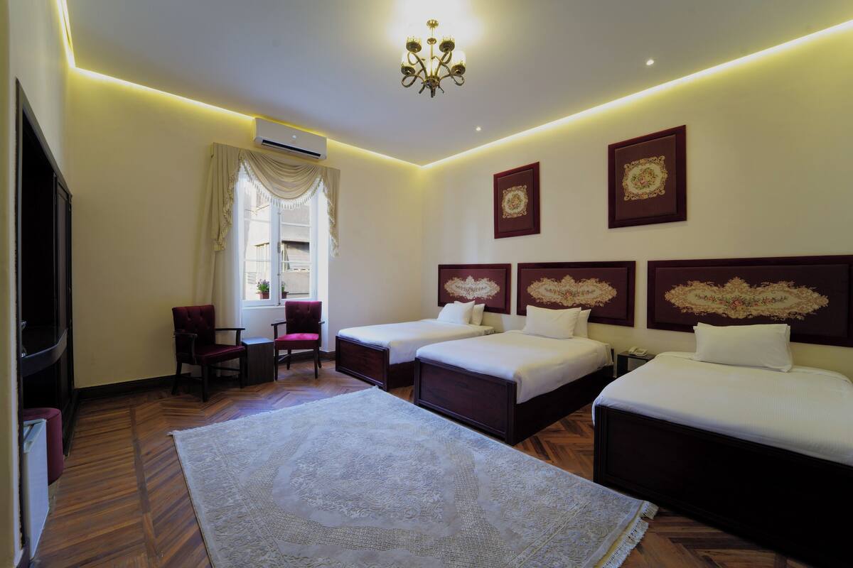 Quarto de hotel com duas camas, uma escrivaninha, uma cadeira e um tapete grande.