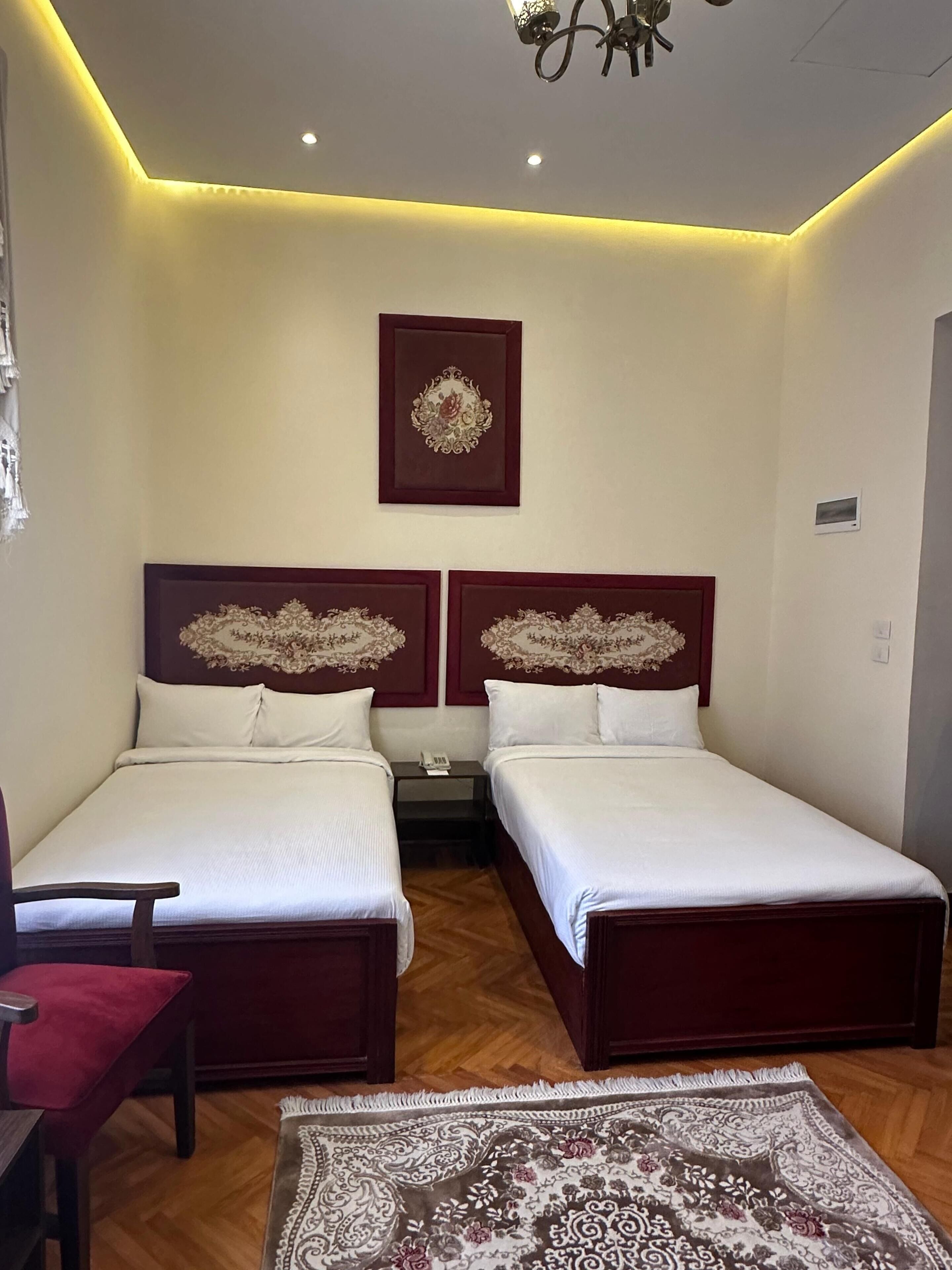 Ein Hotelzimmer mit zwei Betten, einem roten Sessel, einem gemusterten Teppich und einer Wanddekoration.
