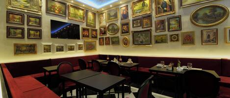 Un restaurante con asientos tapizados en rojo y mesas negras, decorado con cuadros enmarcados en las paredes.