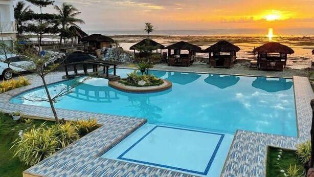Ein Pool mit Blick auf den Sonnenuntergang, Liegestühle und kleine Hütten.