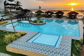 A pool with a view of the sunset, lounge chairs, and small huts. - RedDoorz @ PWL Exclusive Resort Cebu (Carmen)