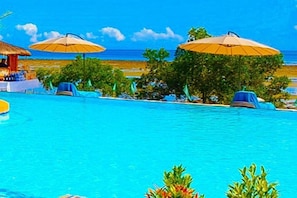 Une piscine entourée de verdure, avec des chaises longues et des parasols, offrant une vue sur la plage.