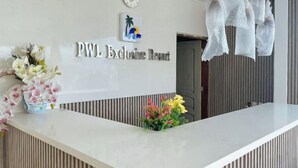 Eine moderne Rezeption im PWL Exclusive Resort mit weißer Arbeitsplatte, dem Logo über dem Namen und dekorativen Blumen.