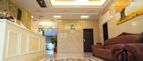 A hotel lobby with a reception desk, a sofa, a chandelier, and a patterned floor.