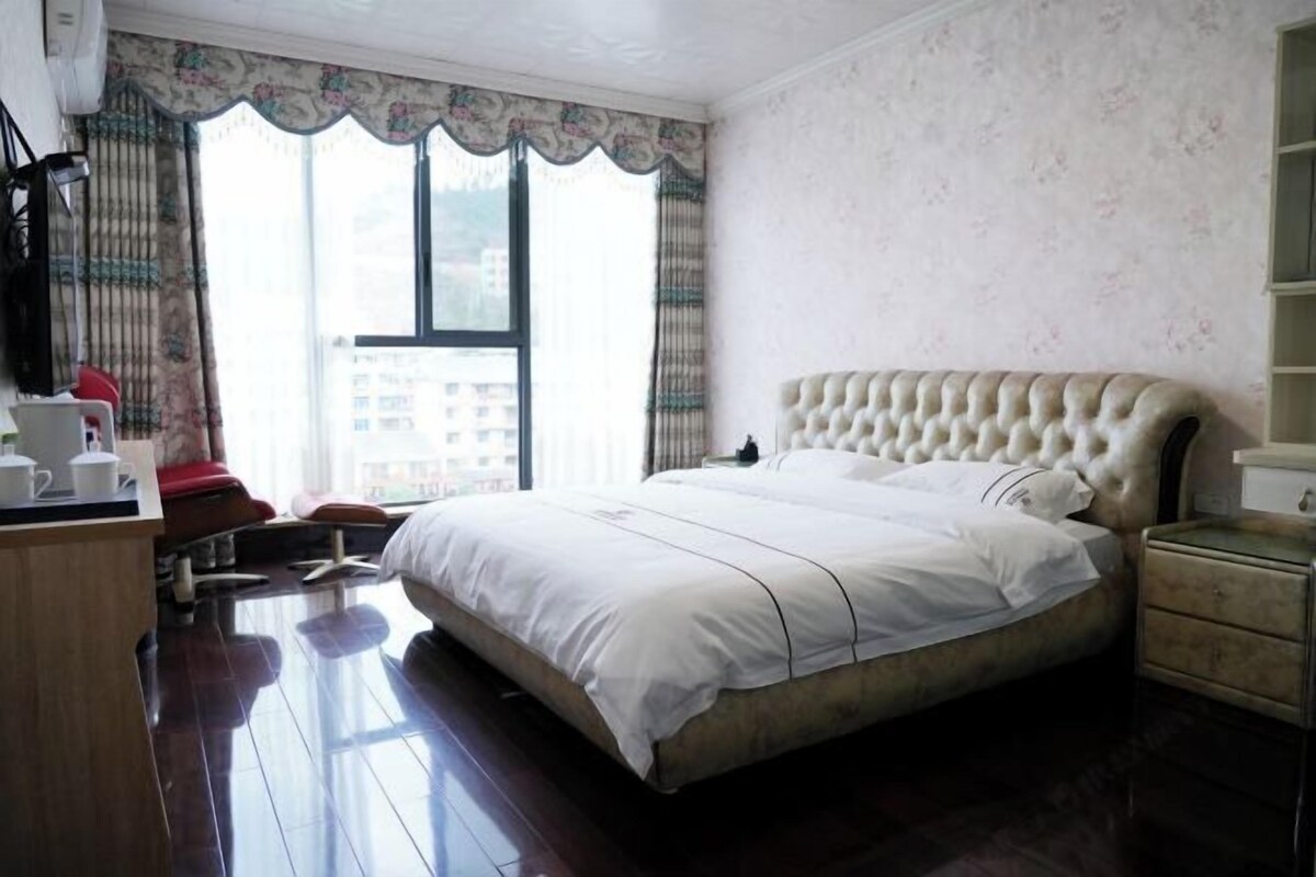 Un dormitorio con una cama grande, un escritorio de madera, una silla y una ventana con cortinas.