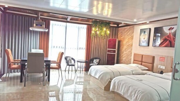 A hotel room with a bed, a desk, chairs, a small table, a plant, and a view of the outdoors. - Xuan'en Junhua Hotel (Xuan'en)