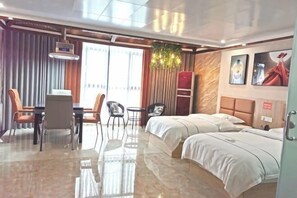 A hotel room with a bed, a desk, chairs, a small table, a plant, and a view of the outdoors. - Xuan'en Junhua Hotel (Xuan'en)