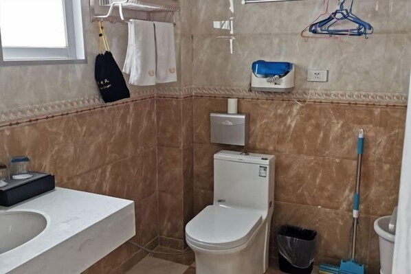 A bathroom with a toilet, sink, and a trash bin. - Xuan'en Junhua Hotel (Xuan'en)
